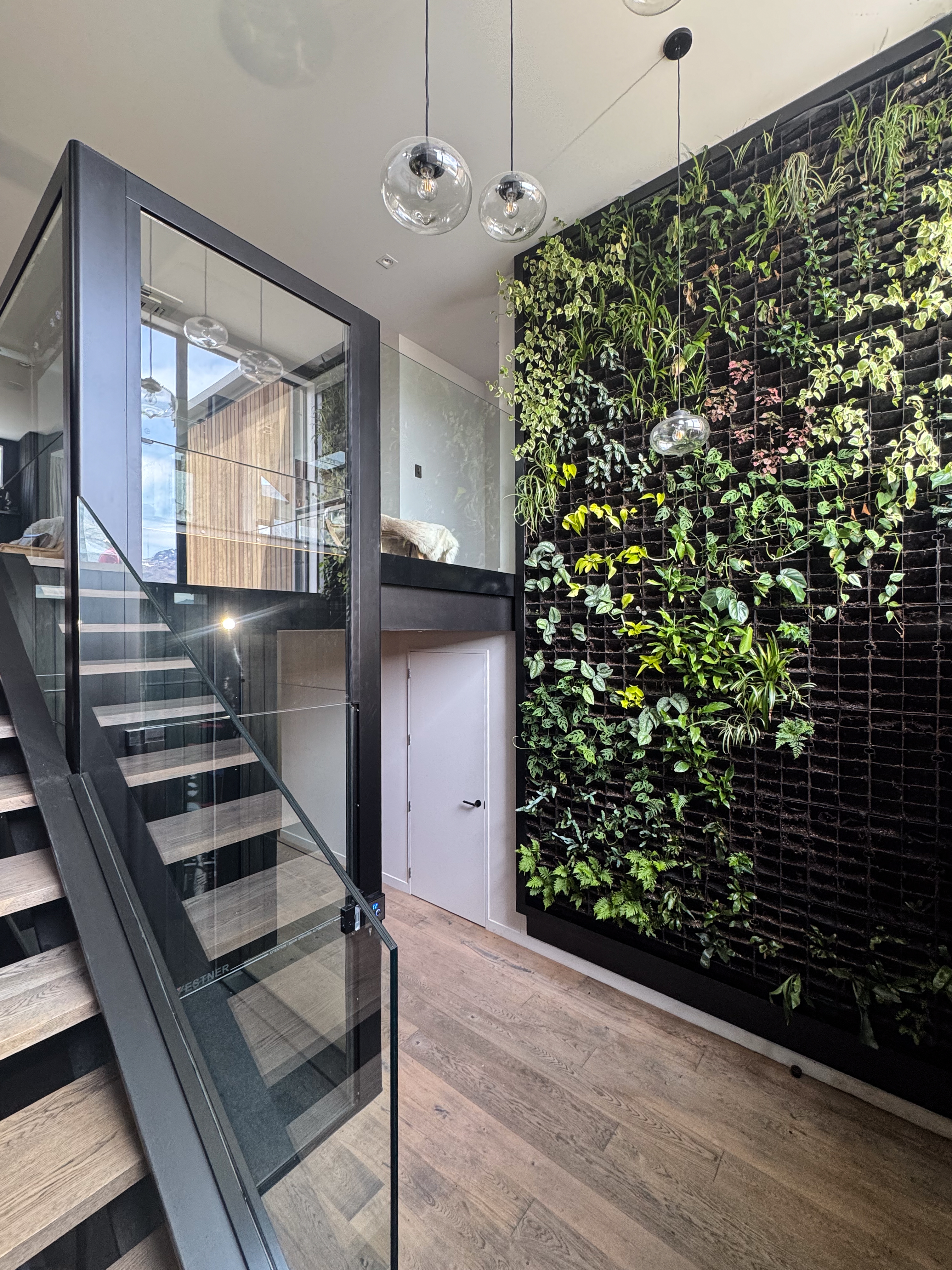 Stairwell with glass-sided Vestner lift, indoor living green wall and glass globe pendant lights